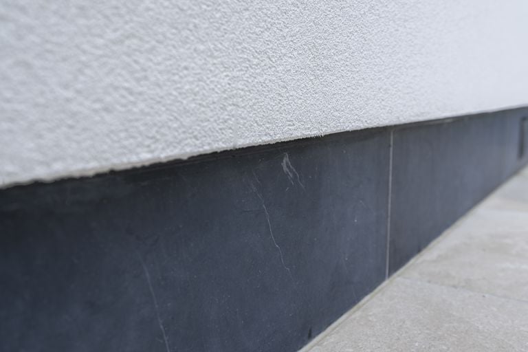 Gevelplint in blauwe steen onder witte crepi